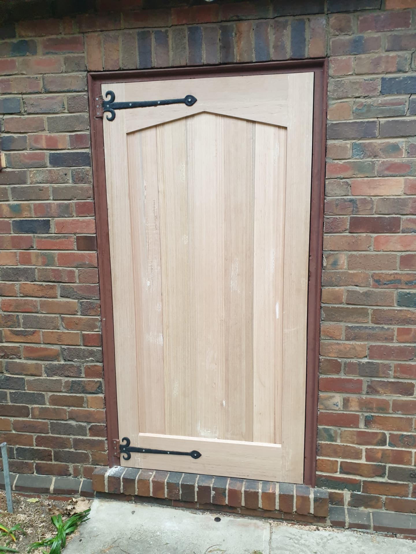 Custom hardwood arched gate door with wrought iron hinges in a brick wall
