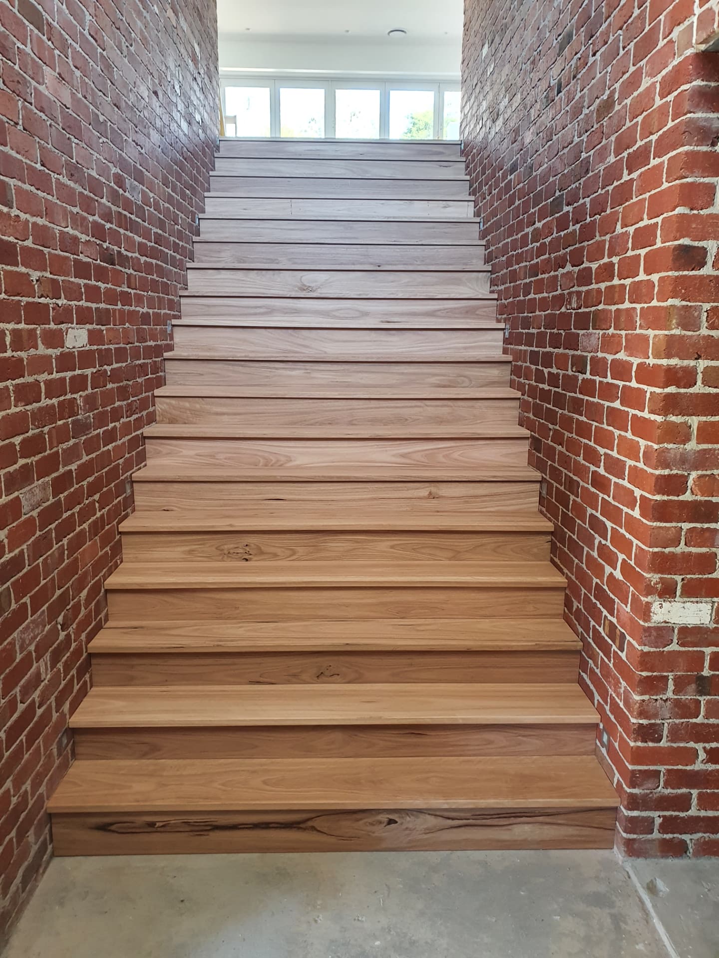 Solid timber staircase between exposed brick walls